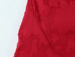 Macro de tissu jacquard rouge montrant des motifs floraux et des textures frangées