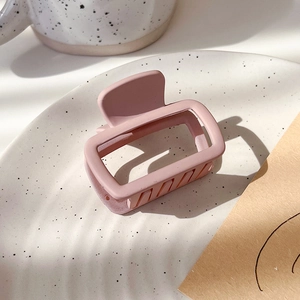 Close-up of matte pink square hair claw clip on decorative ceramic plate in natural light