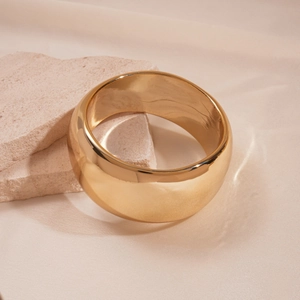 Close-up of wide polished gold metal cuff bracelet on natural stone with warm lighting