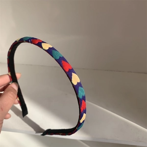 Detail of dark blue fabric headband with colorful hearts held against white background