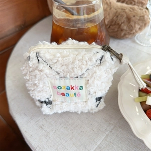 Detail shot of the white plush cosmetic pouch with sozakka beaute embroidered tag