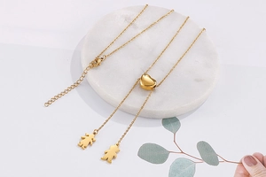 Détail d'un collier cœur doré avec pendentifs garçon et fille sur plateau en marbre