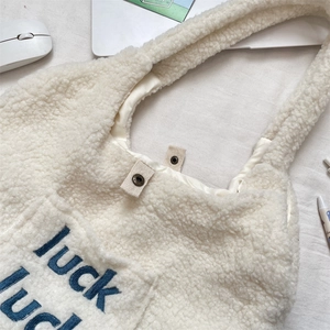 Detail of magnetic buckle closure on white fleece tote bag with luck embroidery