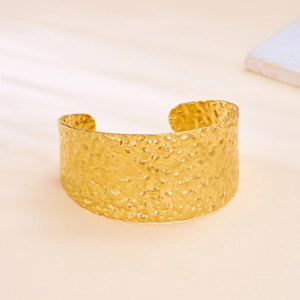Detail of wide open gold cuff bracelet showing hammered metal texture and irregular pattern