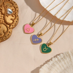 Detailed view of three gold heart necklaces with pink, purple and green zodiac symbols