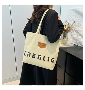 Detail of off-white canvas tote bag with black logo and brown leather shield patch