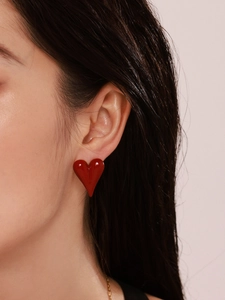 Close-up of a model wearing vibrant red heart-shaped stud earrings with a glossy finish