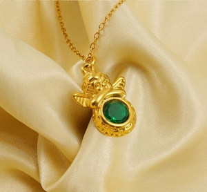 Gros plan détaillé du pendentif ange doré avec zircon vert sur tissu en soie dorée