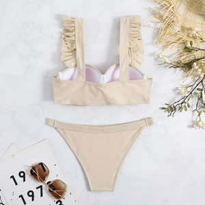 Flat lay of beige two-piece bikini with ruffled straps on white marble surface
