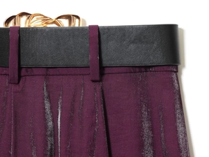 Nahaufnahme von dunkelviolettem Metallic-Stoff mit schwarzem Ledergürtel und Golddetails