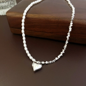 Détail du collier asymétrique en perles et pendentif cœur argenté sur support en cuir