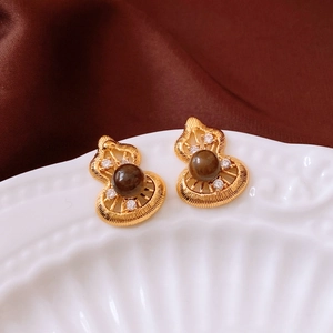 Close-up of golden gourd earrings with dark brown beads and crystals on satin