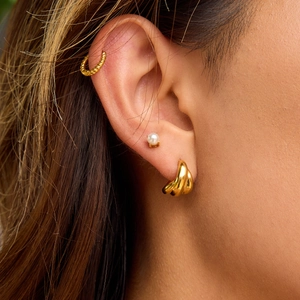 Three-piece gold pearl earring set featuring textured hoops and a lustrous stud on model