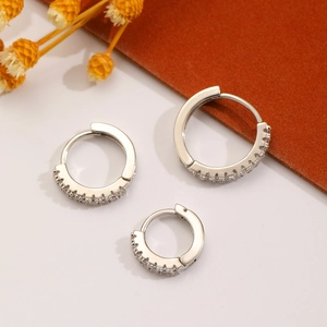 Three silver alloy hoop earrings with white zircon inlays on leather background