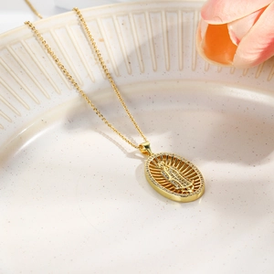 Macro view of gold-plated Virgin Mary pendant with cubic zirconia on white ceramic tray