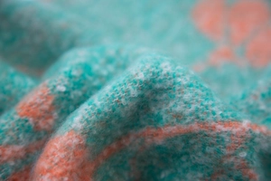 Detailed macro view of soft turquoise and orange floral jacquard knit texture with fringe