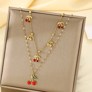 Double-layer gold stainless steel necklace with red cherry pendants on silk background