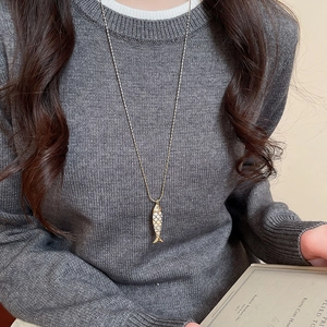 Close-up of a gold fish pendant necklace with white enamel detail on a gray sweater