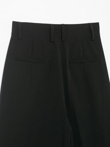 Detail of black casual trousers showing waistband loops and welt back pocket on woven fabric