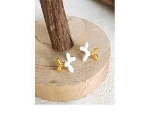 Detail of cute balloon dog earrings with white enamel finish and gold plated accents