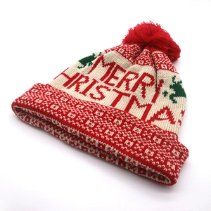Detail of red and white knit Christmas hat featuring Merry Christmas pattern and pom-pom