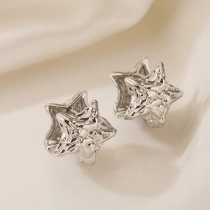 Silver star earrings with irregular folded metal texture on soft white fabric background