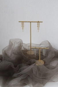 Close-up of elegant gold and silver long tassel earrings on a sleek metal display stand