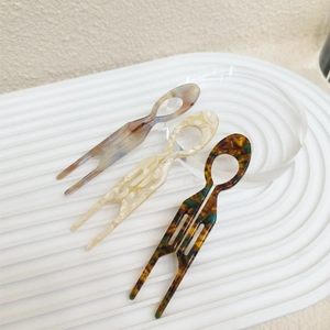 Macro view of acetate U-shaped hair pins in tortoise and marble patterns on textured stand