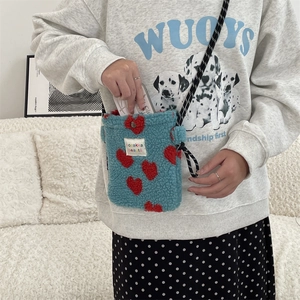 Close-up of blue plush heart crossbody bag with red pattern and black rope strap