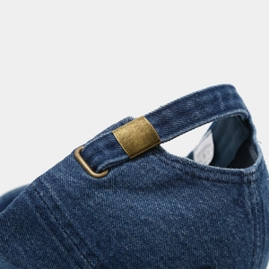 Detail view of the vintage copper metal buckle and washed denim strap on the baseball cap