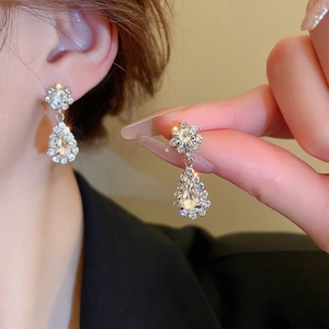 Detail of silver drop earrings with shimmering crystals worn by a model in soft lighting