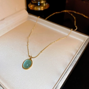 Minimalist gold necklace with oval turquoise pendant displayed in a beige jewelry box