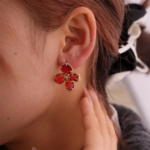 Gros plan de boucles d'oreilles fleur rouge avec bord doré portées par un mannequin