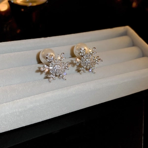 Macro detail of snowflake stud earring with pavé zirconia and white pearl on velvet