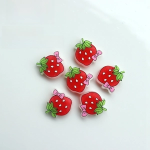 Macro shot of cute resin strawberry charms with pink bows for DIY crafts on a white plate