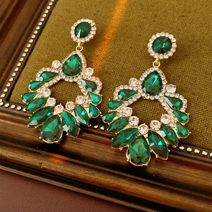 Détail de boucles d'oreilles dorées avec pierres vertes sur cadre en bois vintage
