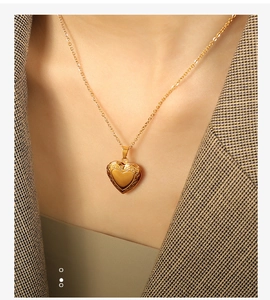 Close-up of a heart-shaped gold locket necklace worn by a model in a dark blazer