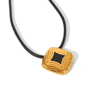 Macro view of gold square pendant with ripple texture and black center on a black cord