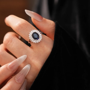 Close-up of sapphire blue oval zircon ring with a diamond halo on a model hand