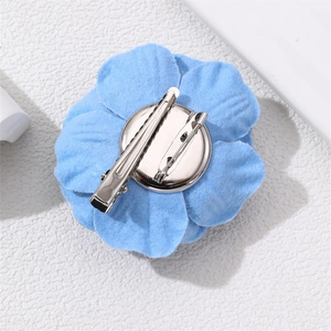 Macro shot of blue denim camellia flower brooch showing the fabric petals and metal clip