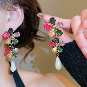 Detail of colorful gemstone flower earrings with a hanging white teardrop pearl drop