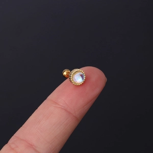 Minimalist gold moonstone stud earring with rainbow glow held on a fingertip