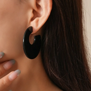 Close-up of a model wearing large black geometric acrylic hoop earrings in a minimalist style
