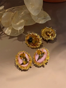 Detailed macro view of vintage oval resin earrings with dried flowers and gold wavy borders