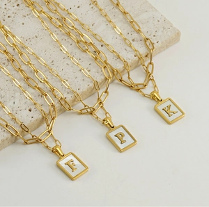 Detail of 18K gold paperclip chain necklaces with white shell square letter pendants