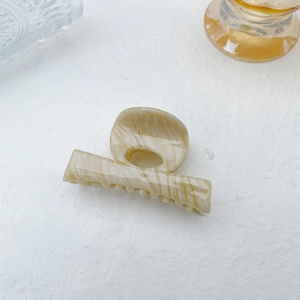 Close-up of beige marble pattern hair claw clip on white textured background