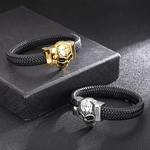 Detail of woven leather bracelets with gold and silver skull charms on a textured black box