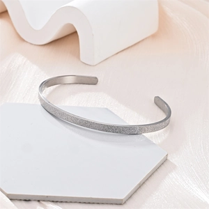 Primer plano de un brazalete abierto en forma de C de acero de titanio plateado mate suave