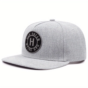Détail d'une casquette snapback grise avec écusson noir circulaire et broderie lettre H