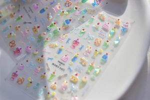 Gros plan de stickers 3D pour ongles dessert avec gâteaux roses, soda et nœuds sur céramique